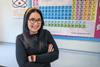 A science teacher standing in front of a periodic table wall poster