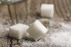 Three sugar cubes on a wooden surface surrounded by sugar granules