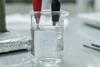 Electrode set-up to anodise titanium in a beaker with red crocodile clip holding titanium and black crocodile clip holding wire in an electrolyte solution