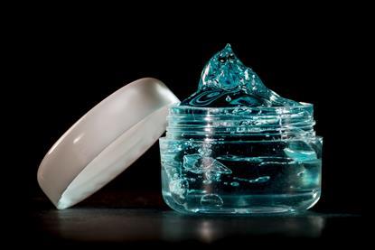 Blue-green hair gel in an opened plastic container against a black background