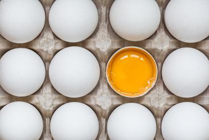 White eggs in a cardboard holder, with one broken in half to reveal the egg yolk and white
