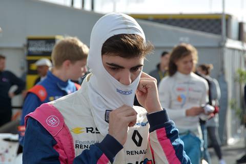 A racing driver preparing for a race pulling on a protective head covering made of nomex before putting on his helmet.