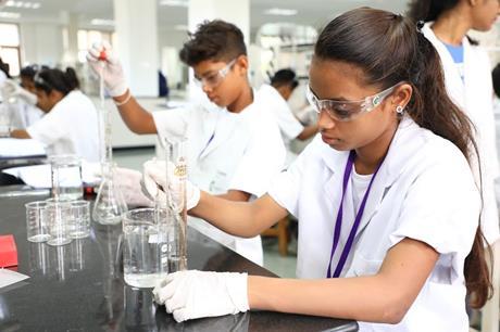 Two students in white lab coats use pipettes to add a clear liquid to glass apparatus